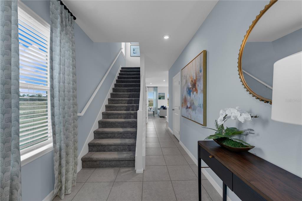 A hallway features light blue walls, gray tile flooring, a carpeted staircase, and wall art — 1938 FAN PALM DRIVE, DAVENPORT, FL