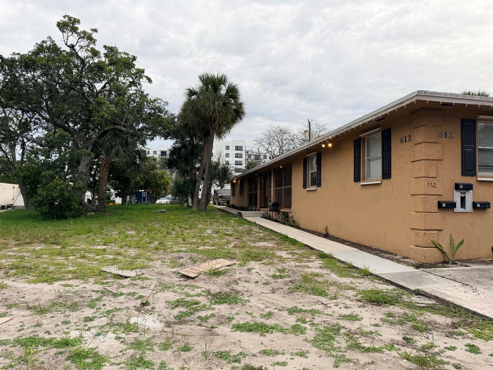 A tan, single-story building with a concrete walkway sits beside a sandy, grassy yard — 612 4th Street, West Palm Beach FL 33401, WEST PALM BEACH, FL