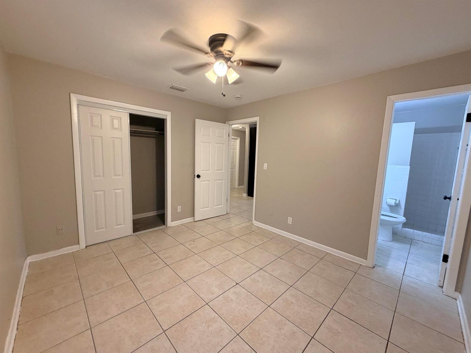 A bedroom with beige walls, tile flooring, a ceiling fan, a closet, and an attached bathroom — 612 4th Street, West Palm Beach FL 33401, WEST PALM BEACH, FL