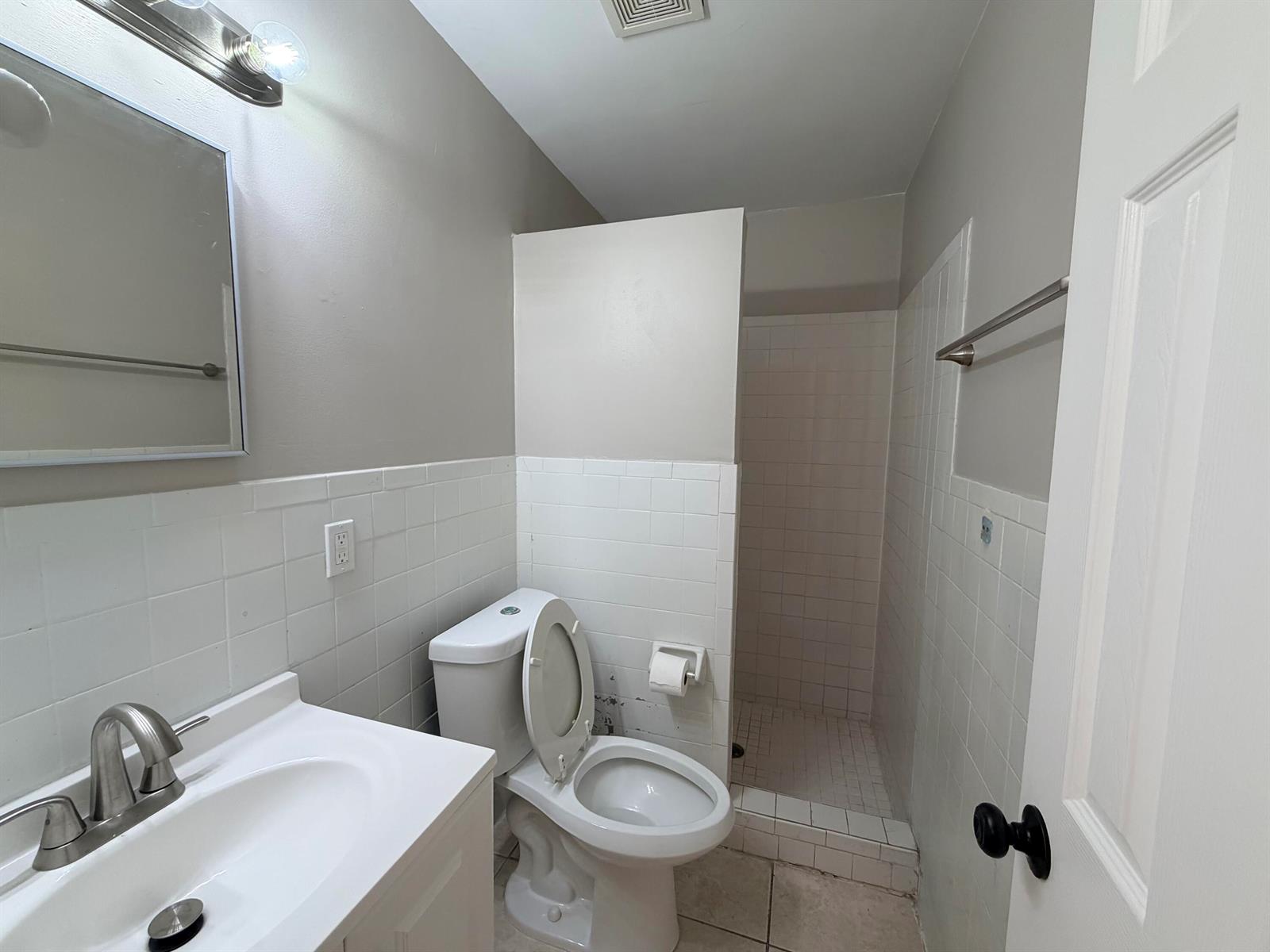 A bathroom features a vanity, toilet, and a tiled shower stall with a half wall — 612 4th Street, West Palm Beach FL 33401, WEST PALM BEACH, FL