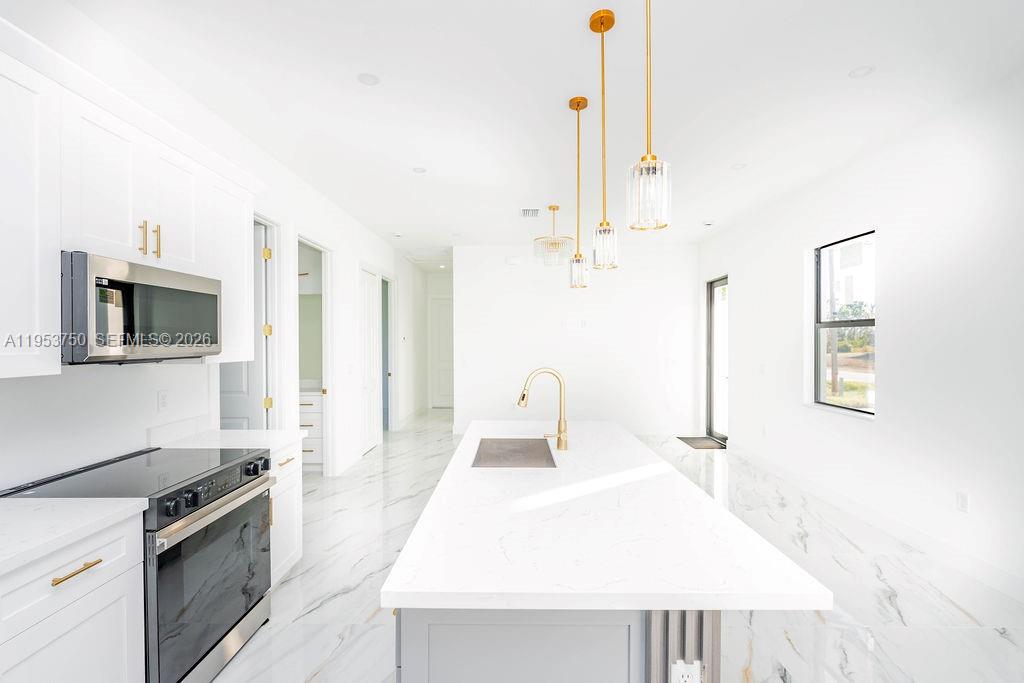 A modern kitchen features white cabinetry, a marble-topped island, and gold pendant lighting — 1005 Brenton Ave, Lehigh Acres FL 33974, LEHIGH ACRES, FL