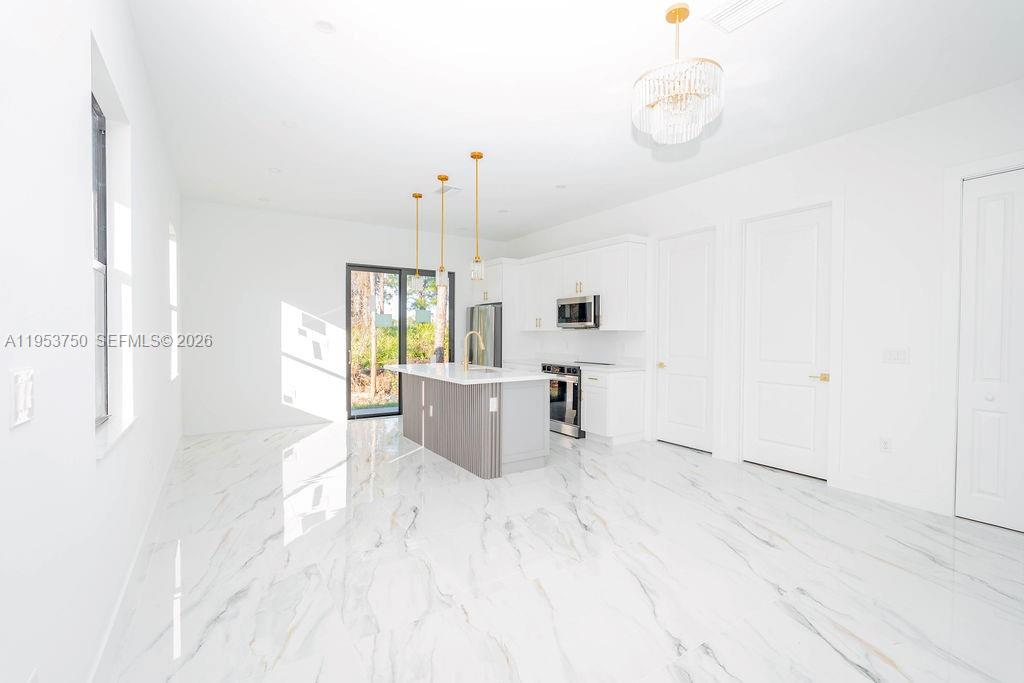 A modern kitchen features white cabinetry, a central island, and white marble-patterned tile flooring — 1005 Brenton Ave, Lehigh Acres FL 33974, LEHIGH ACRES, FL