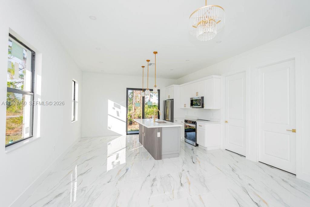 A modern kitchen features white cabinetry, a gray island, and white marble-patterned tile flooring — 1005 Brenton Ave, Lehigh Acres FL 33974, LEHIGH ACRES, FL