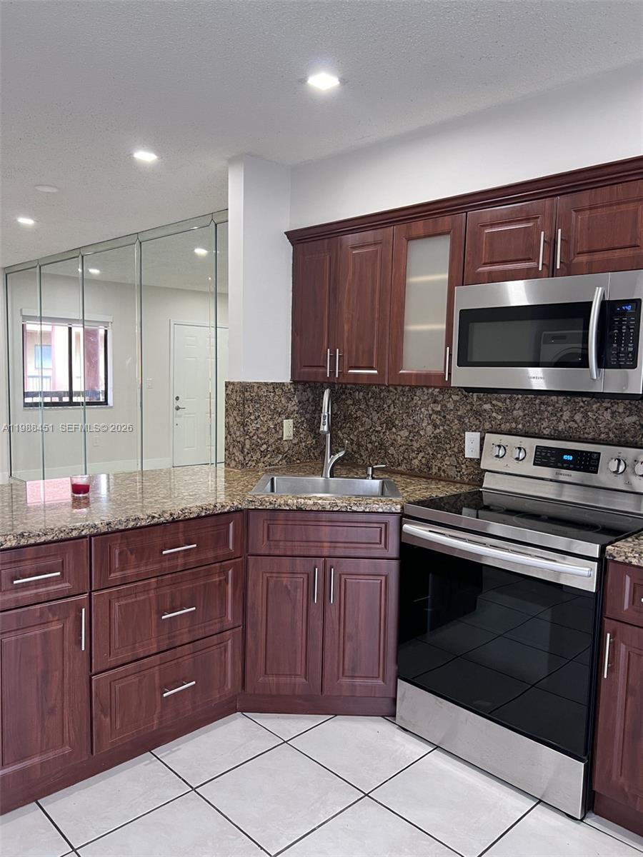 A kitchen features dark wood cabinets, granite countertops, stainless steel appliances, and tiled flooring — 5480 W 21st Ct # 404, Hialeah FL 33016, HIALEAH, FL