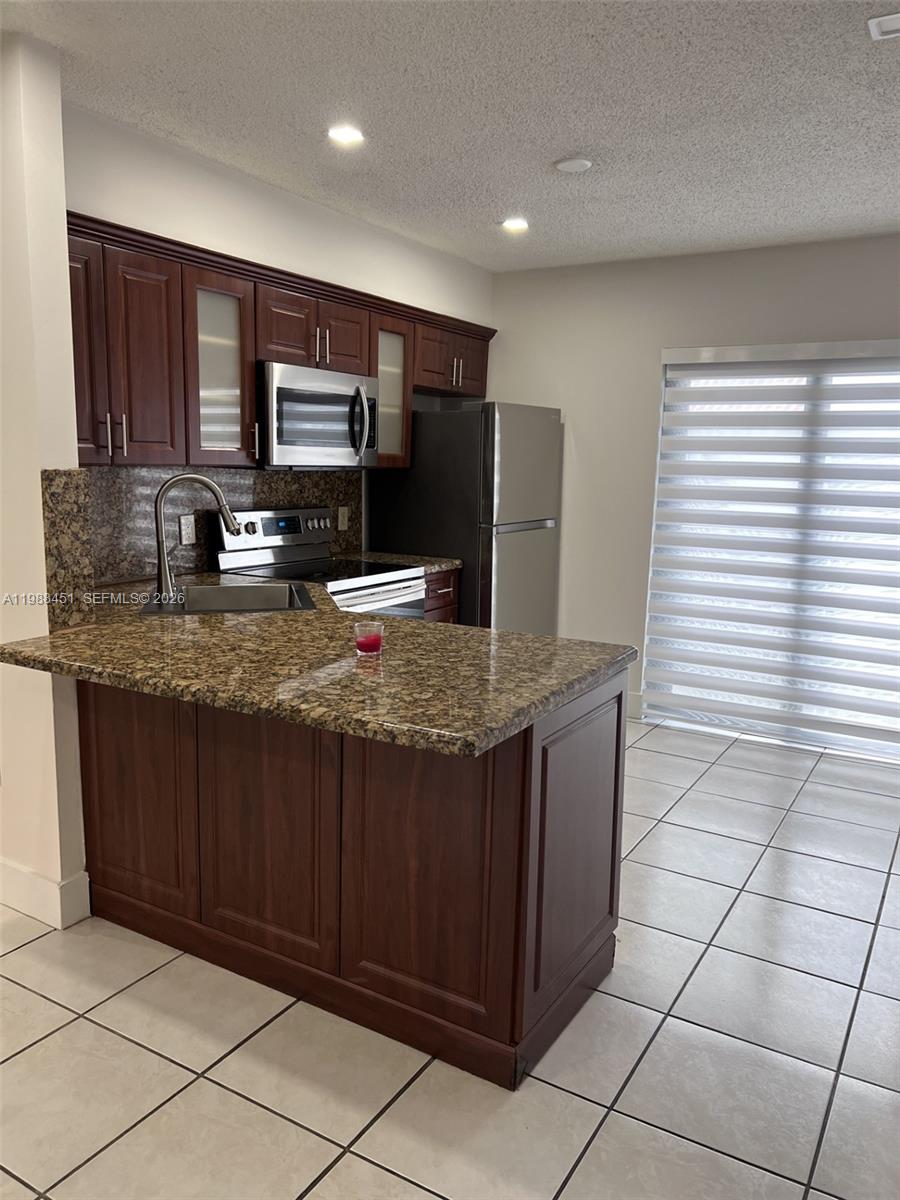 A kitchen features dark wood cabinets, granite countertops, stainless steel appliances, and tile flooring — 5480 W 21st Ct # 404, Hialeah FL 33016, HIALEAH, FL