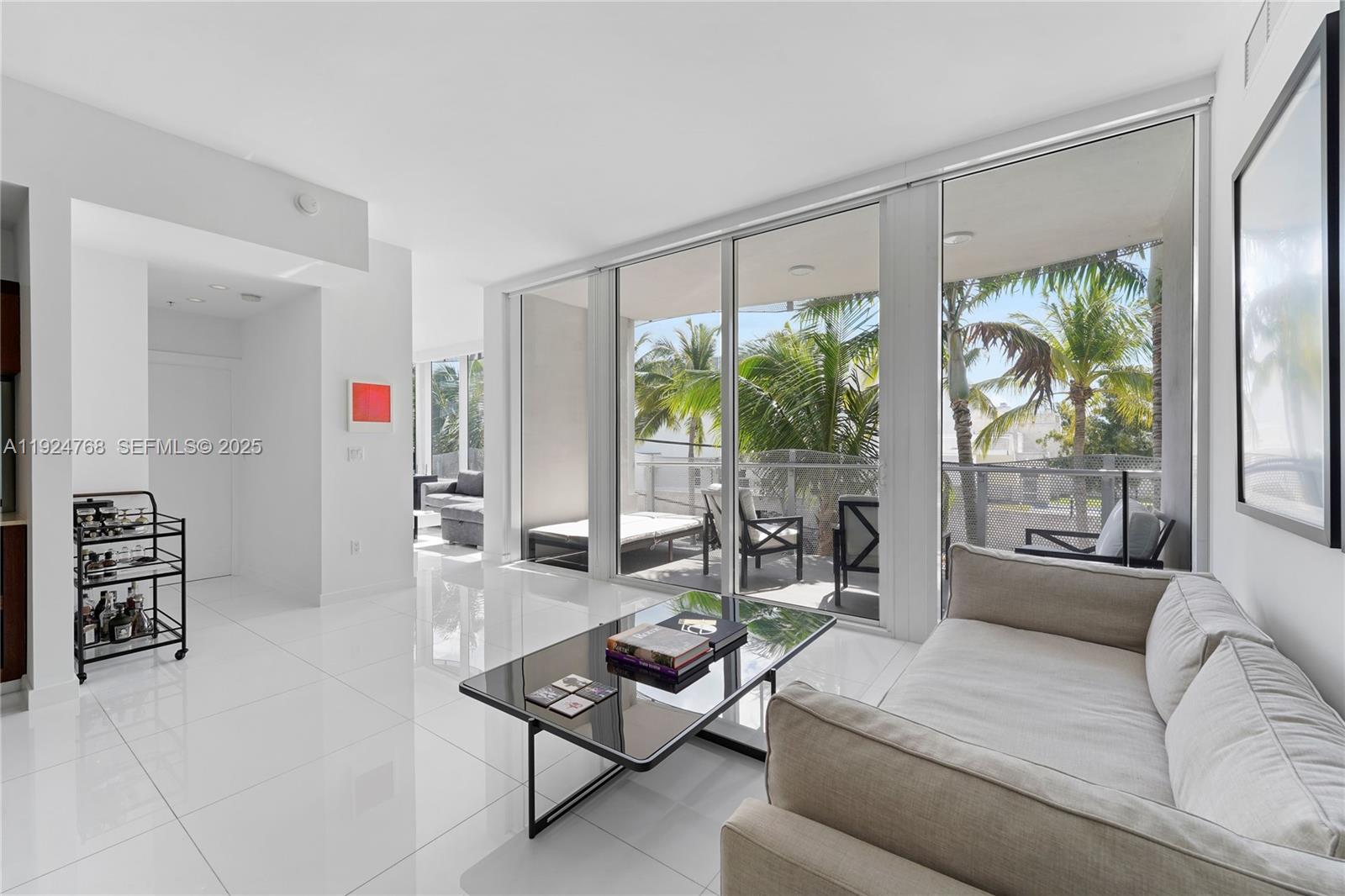 A modern living room features white tile floors, a glass coffee table, and a balcony — 2100 Park Ave # 201, Miami Beach FL 33139, MIAMI BEACH, FL