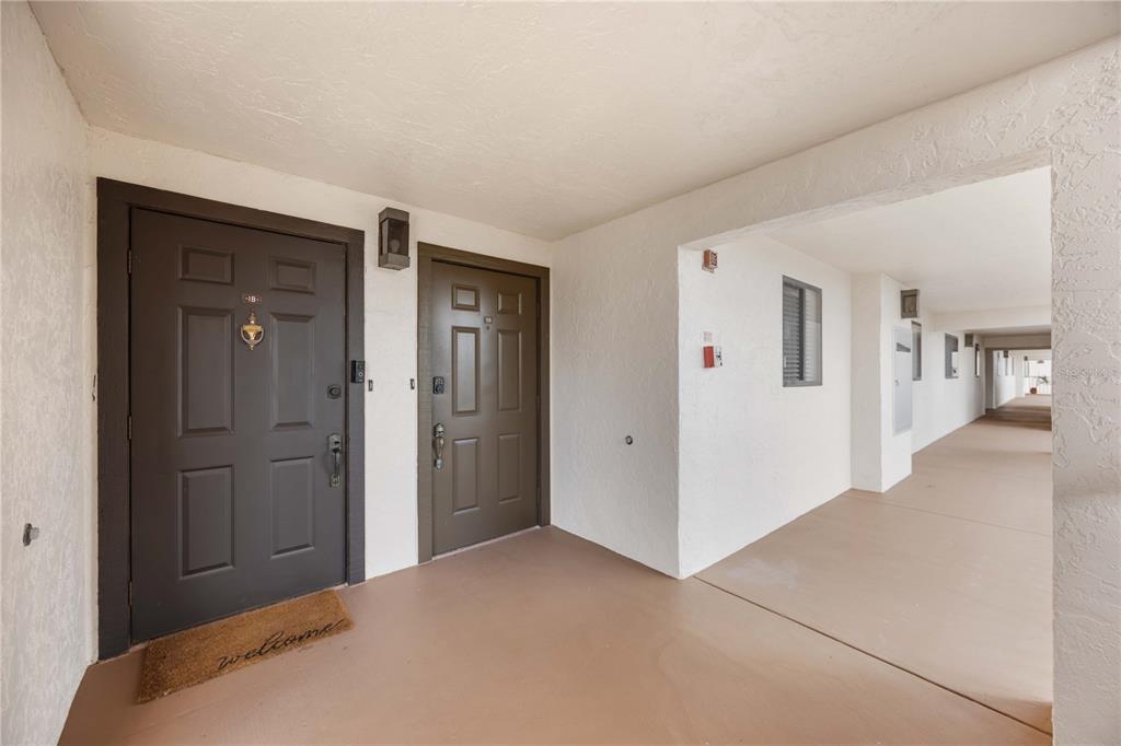 Two brown entry doors are situated side-by-side in a covered outdoor apartment building hallway — 5050 MARIANNE KEY ROAD UNIT 1B, PUNTA GORDA, FL