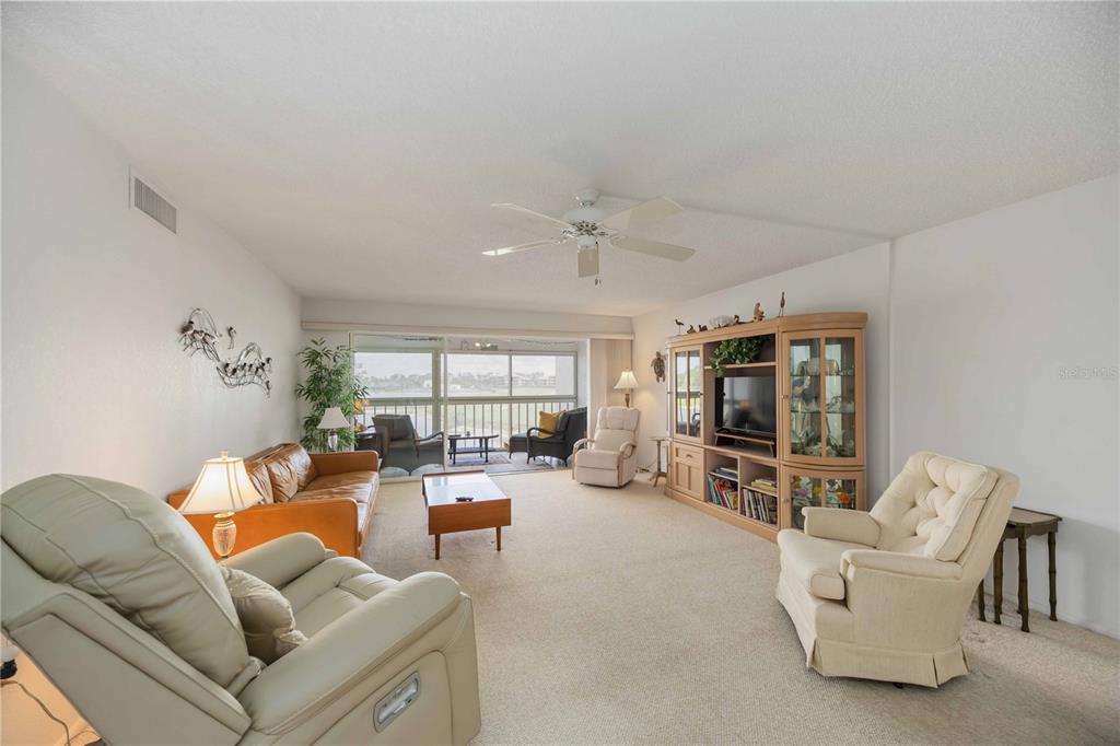 A living room with beige carpet, a large entertainment center, and a sliding glass door — 5050 MARIANNE KEY ROAD UNIT 1B, PUNTA GORDA, FL
