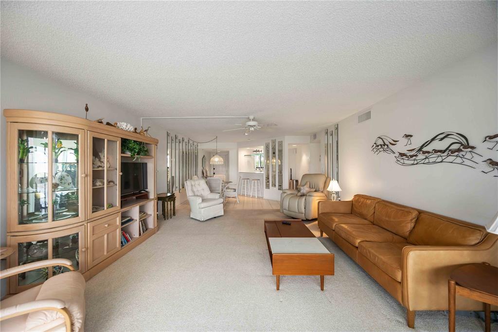 A living room features a tan leather sofa, a large wooden cabinet, and beige carpeting — 5050 MARIANNE KEY ROAD UNIT 1B, PUNTA GORDA, FL