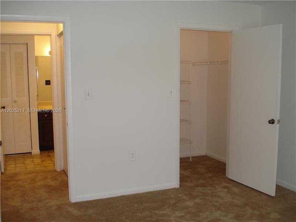 A bedroom interior features beige carpet, a closet with wire shelving, and an adjacent bathroom — 2240 SW 81st Ave # 2240, Miramar FL 33025, MIRAMAR, FL