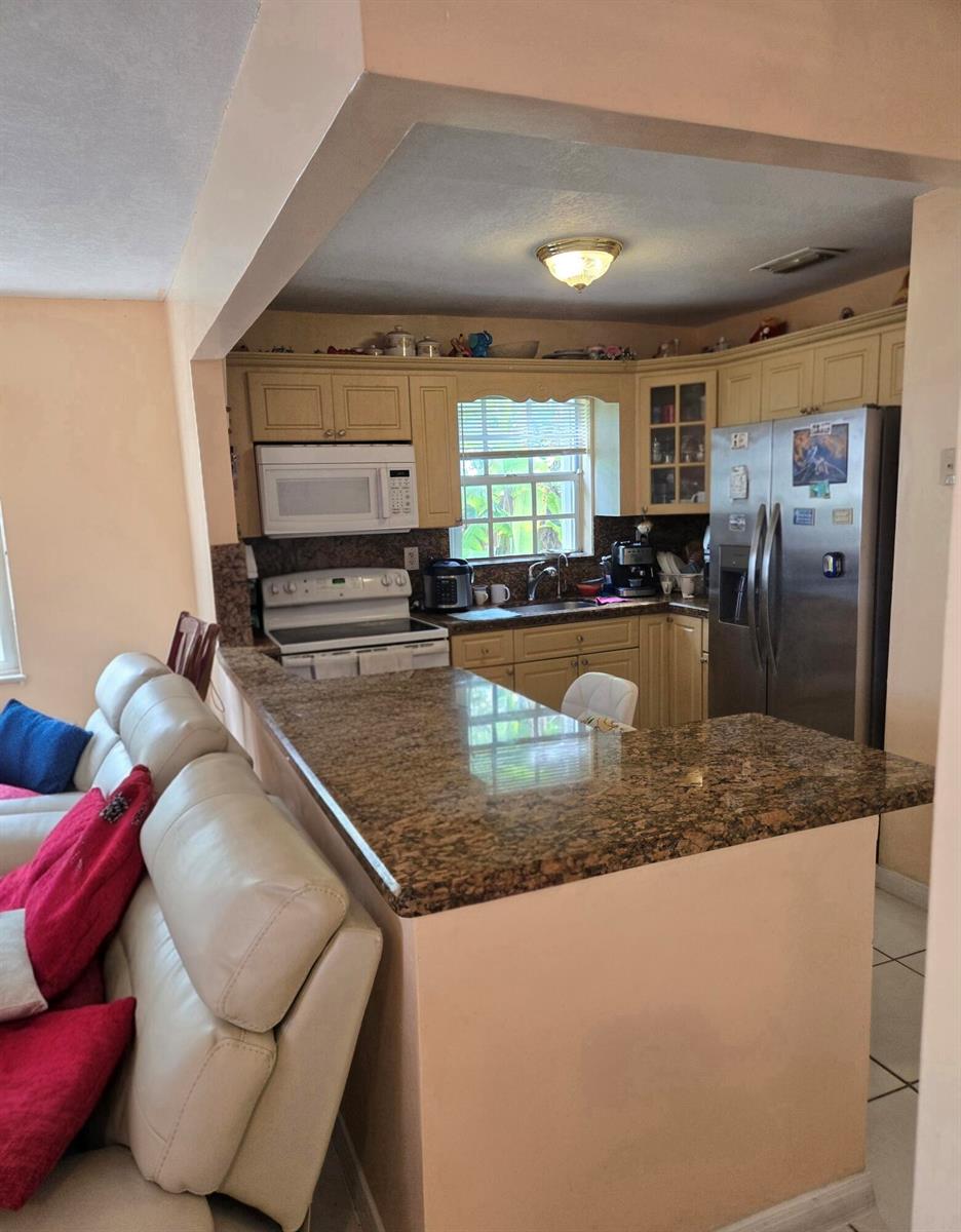 A kitchen with granite countertops and light-colored cabinets overlooks a living area with a sofa — 11302 SW 7th Street, Miami FL 33174, MIAMI, FL