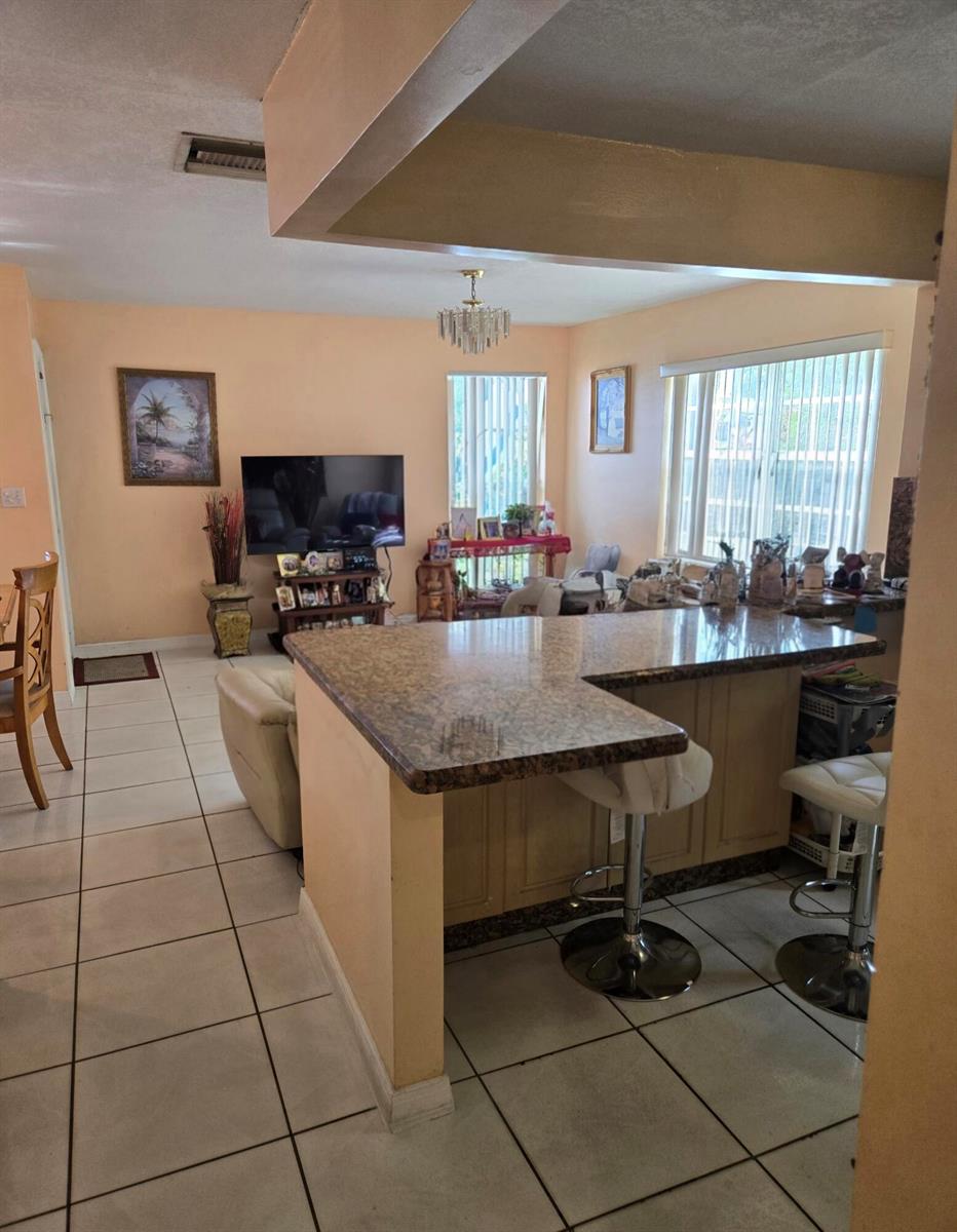 A kitchen with a granite-topped peninsula and bar stools overlooks a living area with tile floors — 11302 SW 7th Street, Miami FL 33174, MIAMI, FL