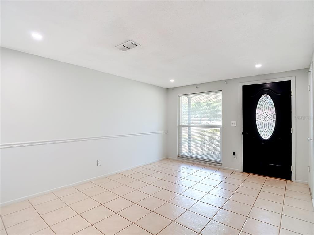 A room with light-colored tile flooring, white walls with chair rail molding, and a black door — 7916 WOODGROVE CIRCLE, TAMPA, FL