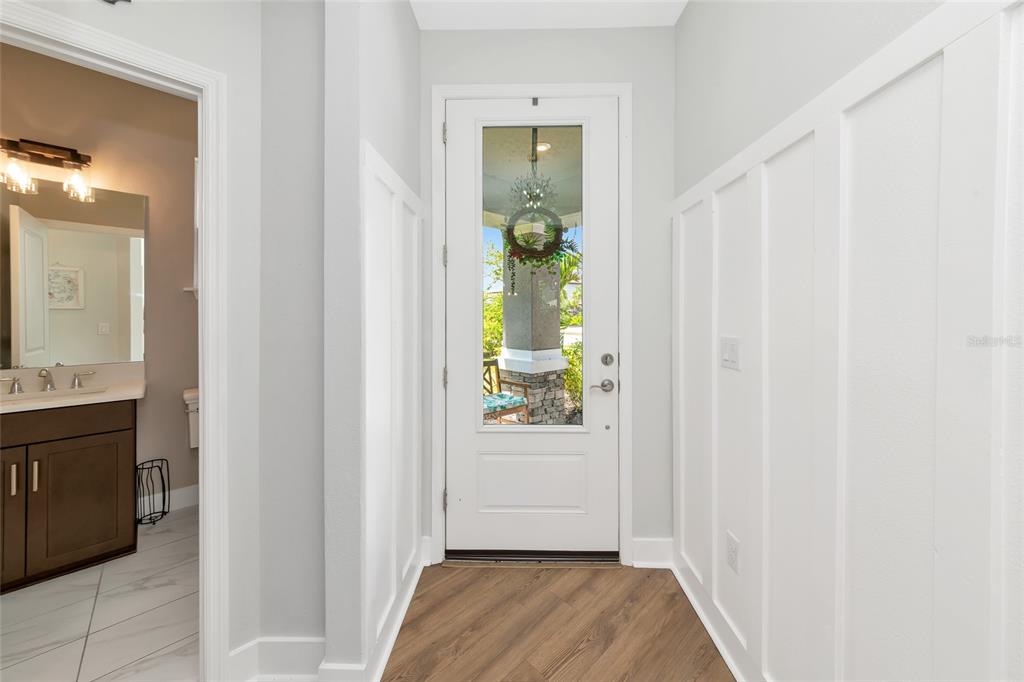 An entryway features white board-and-batten walls, wood-look flooring, and a glass-paneled front door — 8366 VELDA TRAIL, SARASOTA, FL