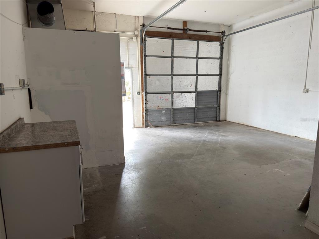 An industrial warehouse space features a concrete floor, white walls, and a large roll-up door — 18290 PAULSON DRIVE UNIT 4, PORT CHARLOTTE, FL