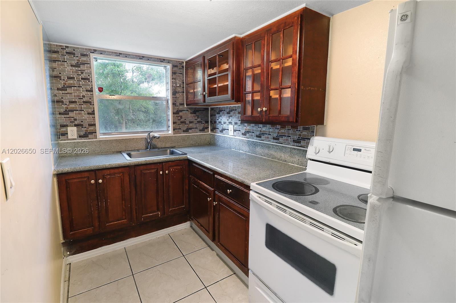 A kitchen features dark wood cabinets, granite countertops, a tiled backsplash, and white appliances — 2235 NW 59th Way # 2235, Lauderhill FL 33313, LAUDERHILL, FL