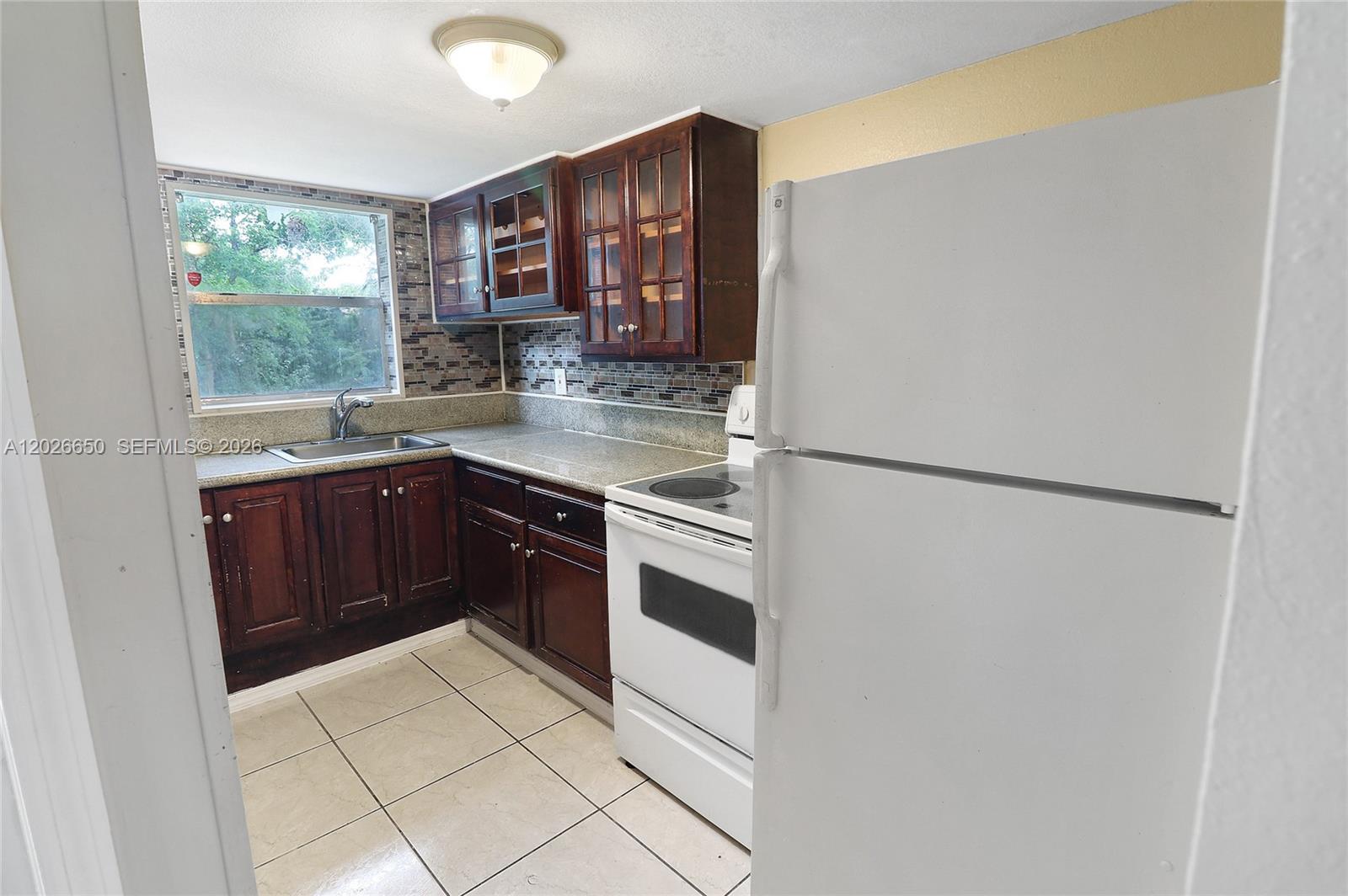 A kitchen features dark wood cabinets, a white stove, a white refrigerator, and tiled flooring — 2235 NW 59th Way # 2235, Lauderhill FL 33313, LAUDERHILL, FL