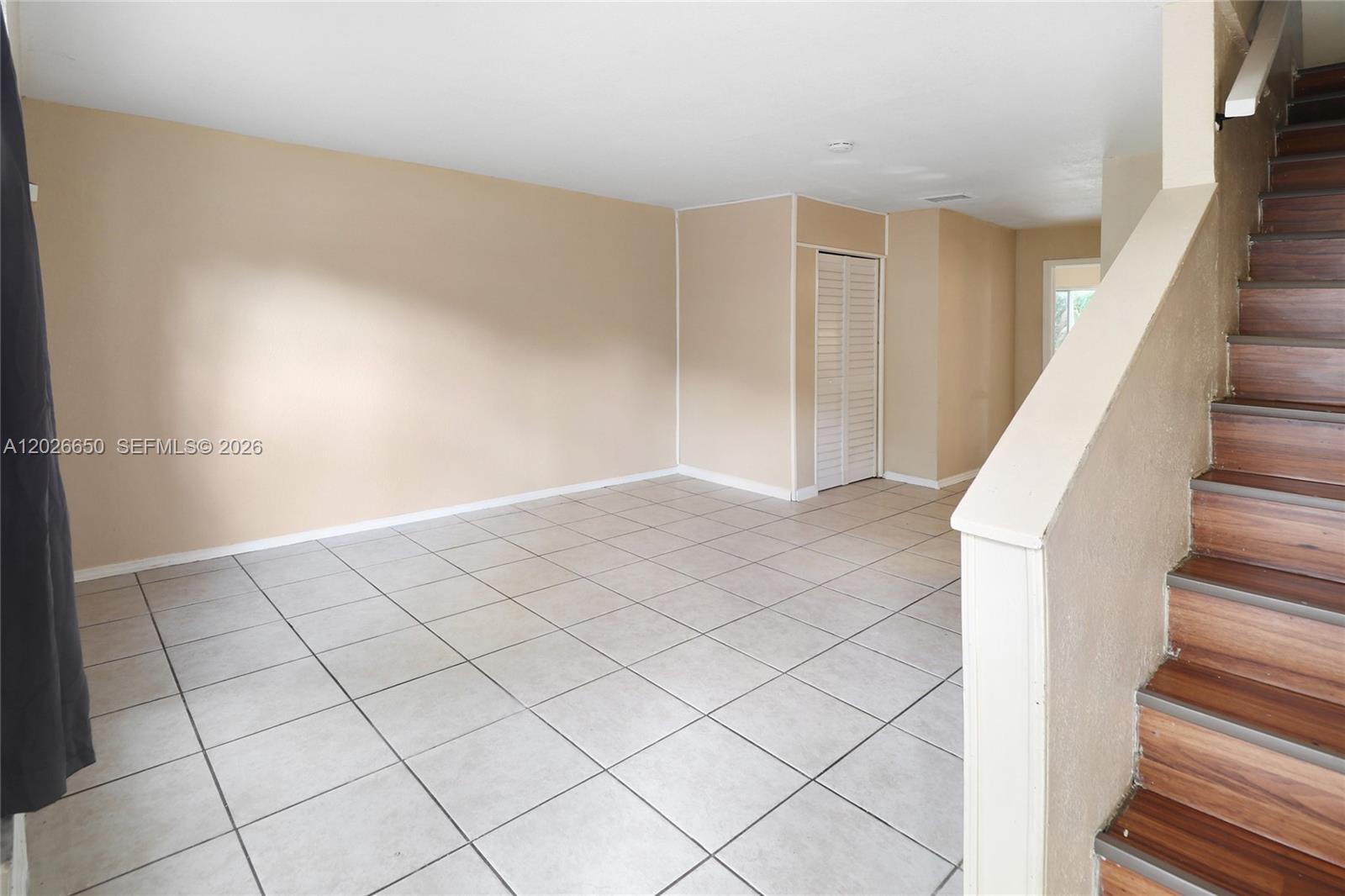 An empty room with beige walls, light-colored tile flooring, and a wooden staircase — 2235 NW 59th Way # 2235, Lauderhill FL 33313, LAUDERHILL, FL