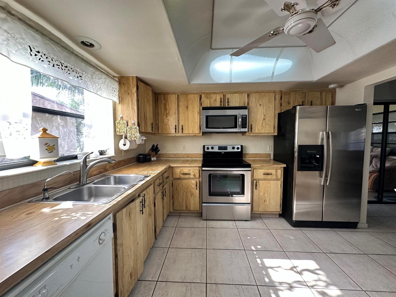 A kitchen features light wood cabinets, stainless steel appliances, laminate countertops, and tile flooring — 6273 Tall Cypress Circle, FL 33463, FL