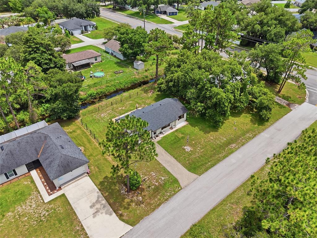 An aerial view shows two houses with dark shingled roofs, driveways, and a grassy yard — 3672 RONDA DRIVE, DELTONA, FL