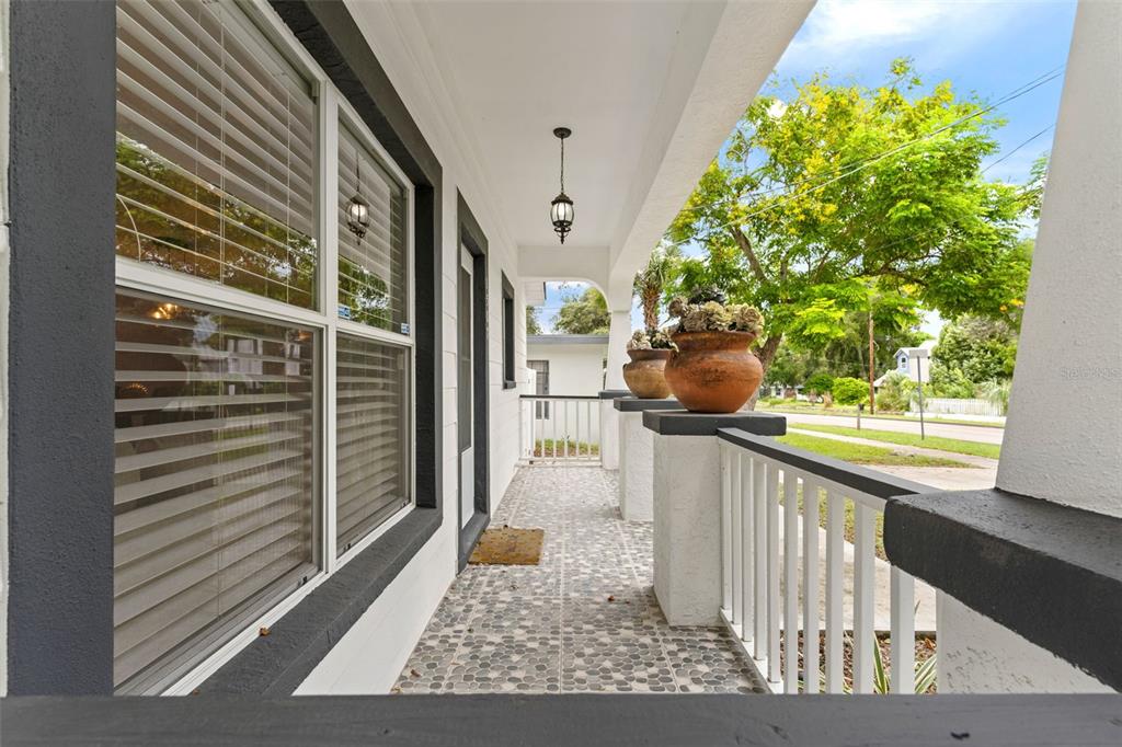 A covered front porch features a pebble-tiled floor, white railings, and two potted plants — 1507 E HENRY AVENUE, TAMPA, FL