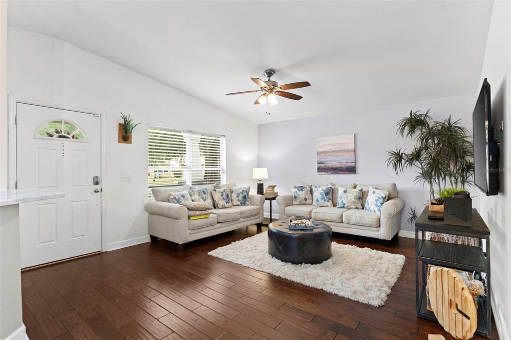 A living room features light-colored sofas, a dark leather ottoman, and wood flooring — 1507 E HENRY AVENUE, TAMPA, FL