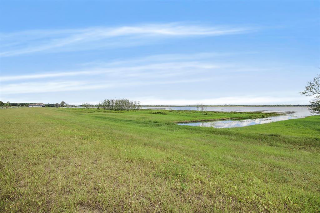 A grassy field slopes down toward a lake under a blue sky with light clouds — 288 CALADIUM AVENUE, LAKE ALFRED, FL