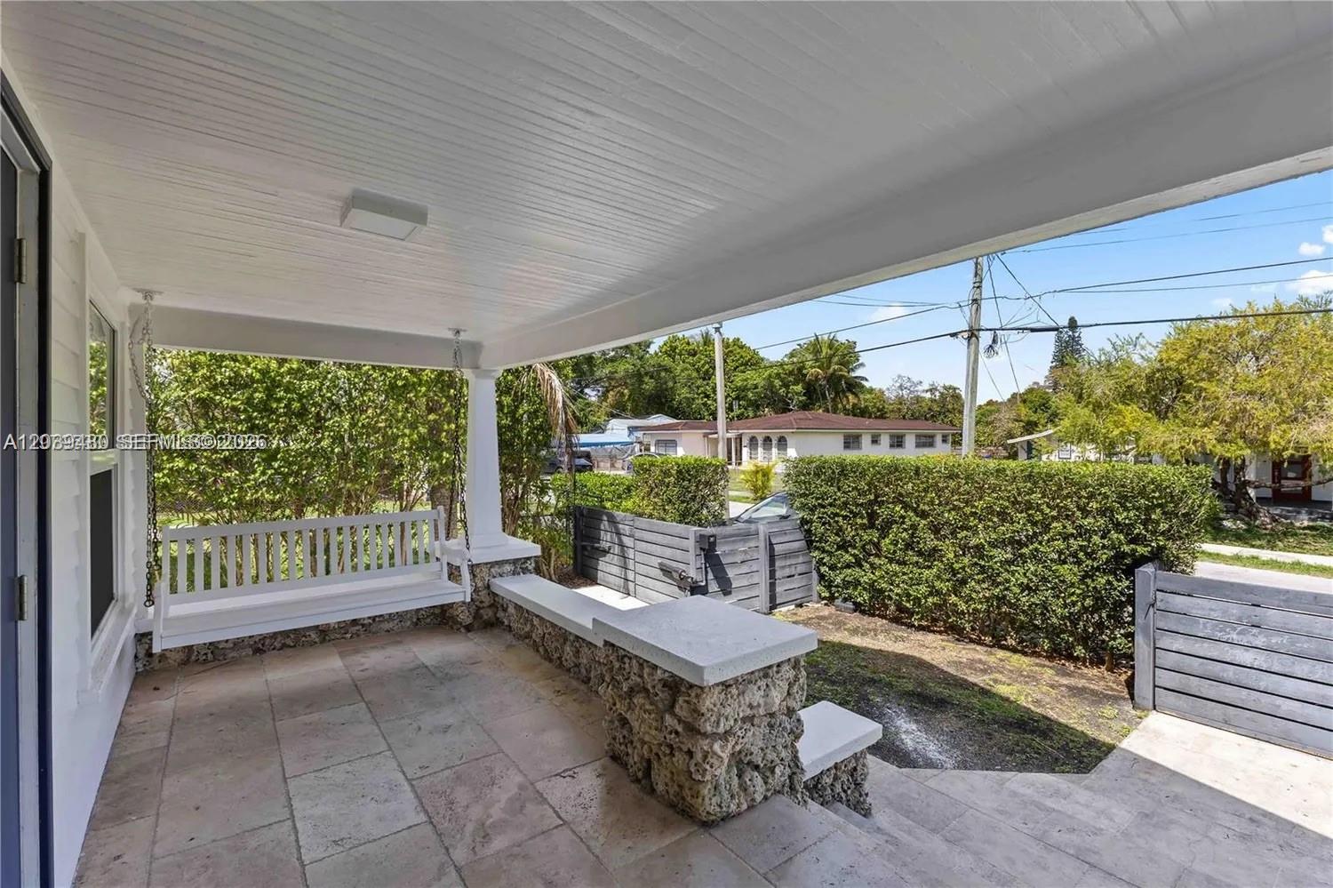 A covered porch features a white hanging bench, stone masonry accents, and tiled flooring — 2434 SW 15th St # 2434, Miami FL 33145, MIAMI, FL