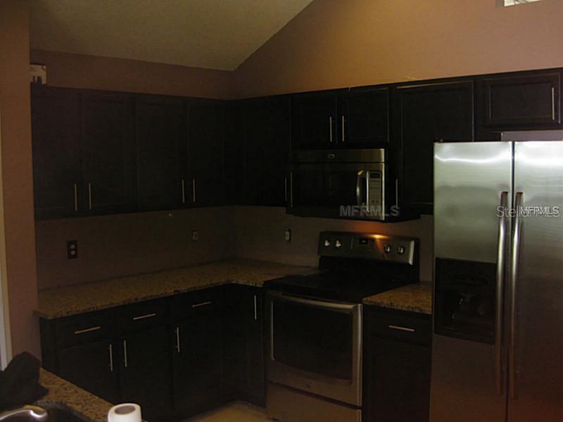 A kitchen features dark wood cabinets, granite countertops, and stainless steel appliances — 4032 BOLINAS COURT, ORLANDO, FL