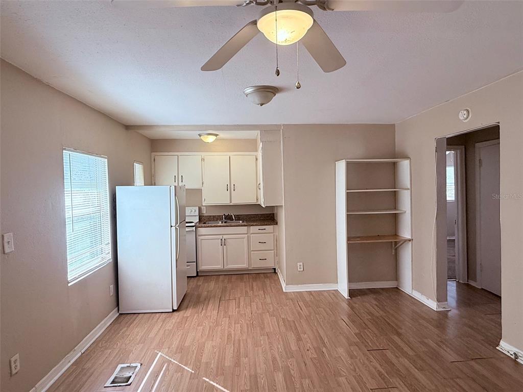 A kitchen with white cabinets, a refrigerator, and wood-look flooring opens to a living area — 986 22ND AVENUE S UNIT 3, ST PETERSBURG, FL