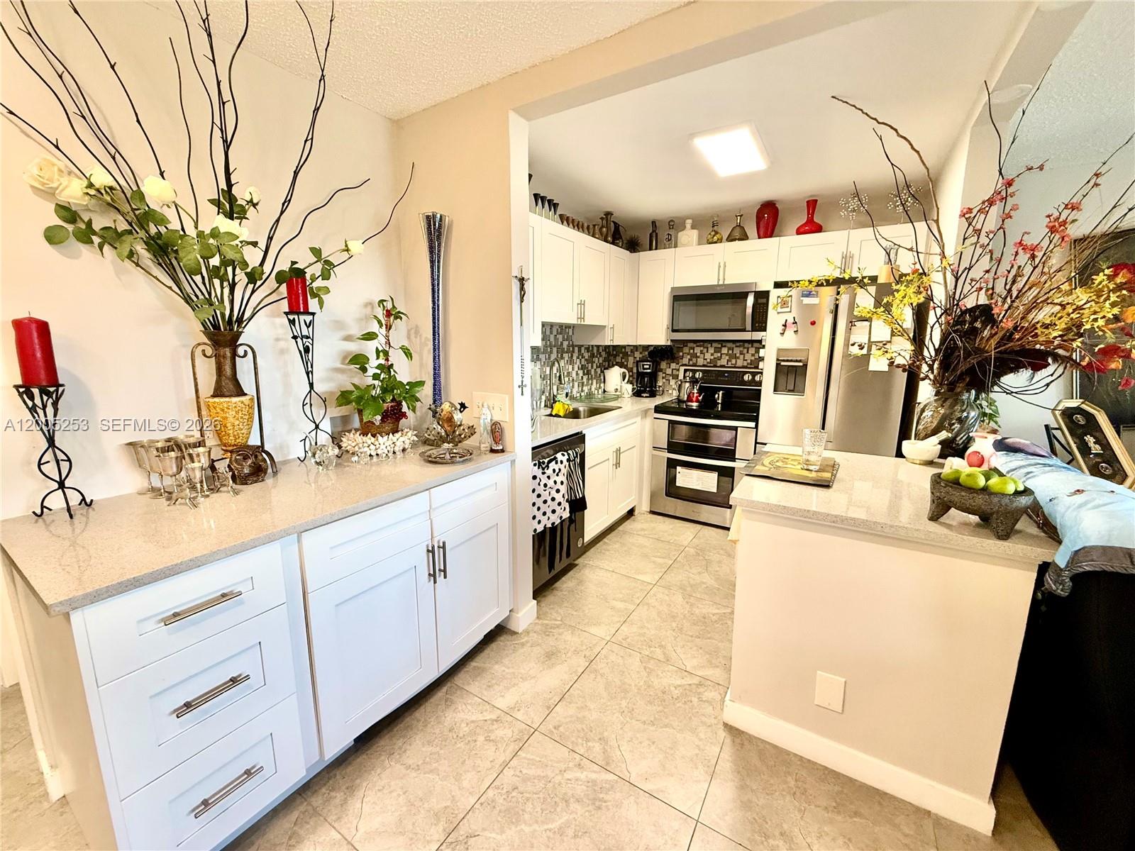 A kitchen features white cabinetry, stainless steel appliances, and a light-colored stone countertop — 431 Chatham U # U, West Palm Beach FL 33417, WEST PALM BEACH, FL