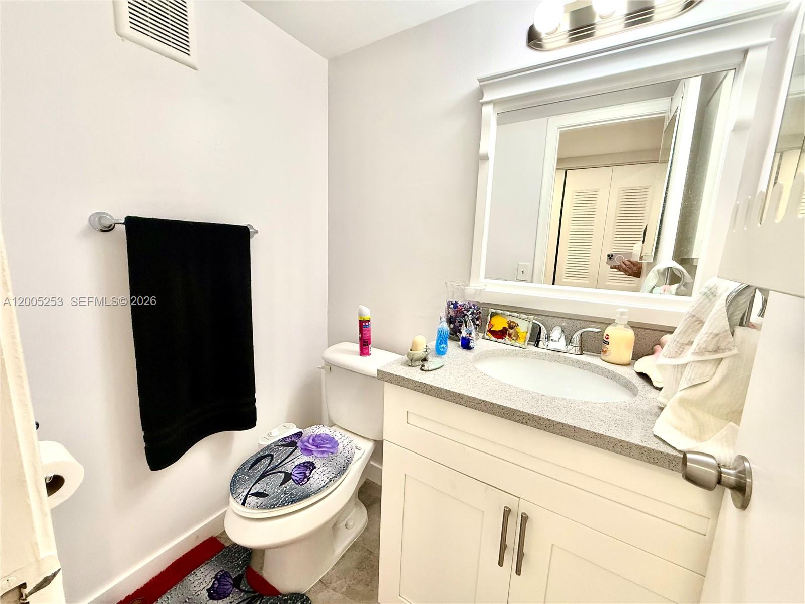 A small bathroom features a white vanity, a toilet with a decorative seat, and a mirror — 431 Chatham U # U, West Palm Beach FL 33417, WEST PALM BEACH, FL