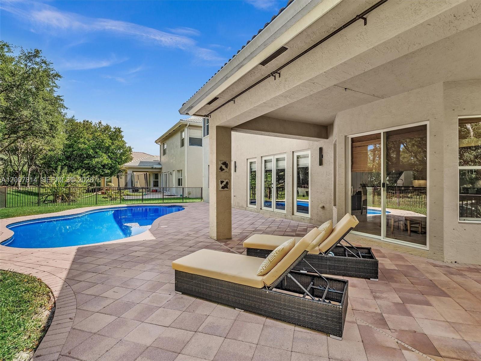 A patio with two lounge chairs overlooks a swimming pool and a fenced backyard — 4961 SW 173rd Ave, Miramar FL 33029, MIRAMAR, FL