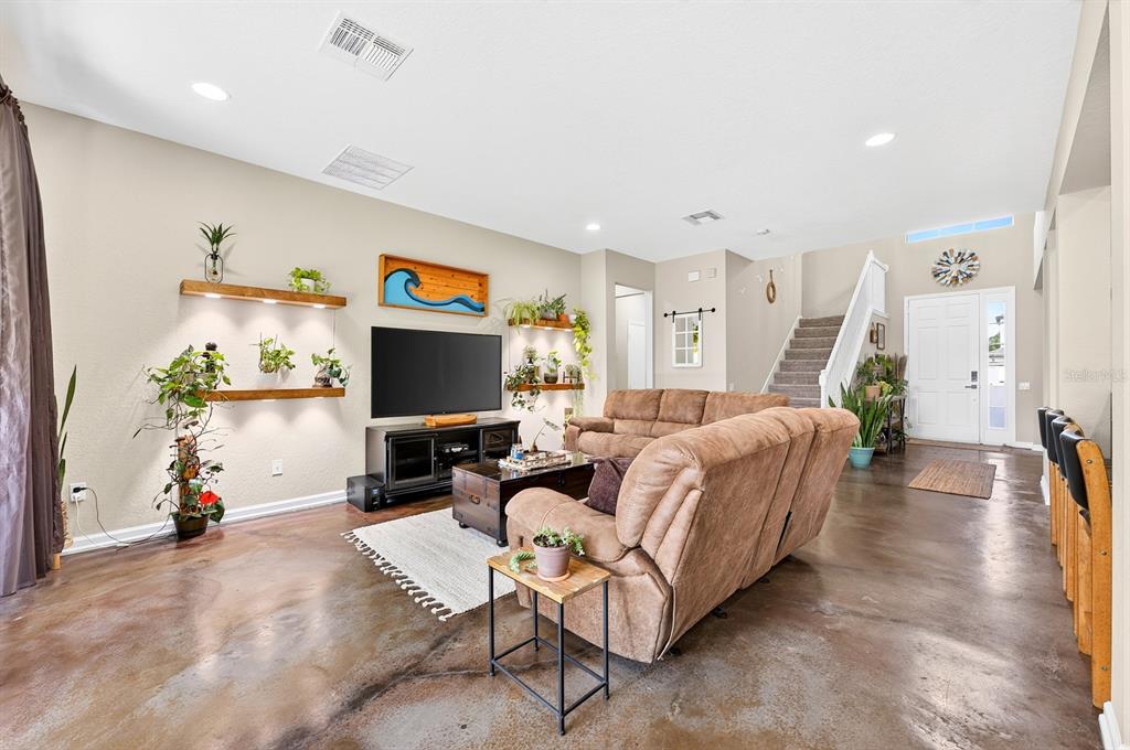 A living room features stained concrete floors, a brown sectional sofa, and wall-mounted floating shelves — 1135 TOLUKE POINT, ORLANDO, FL