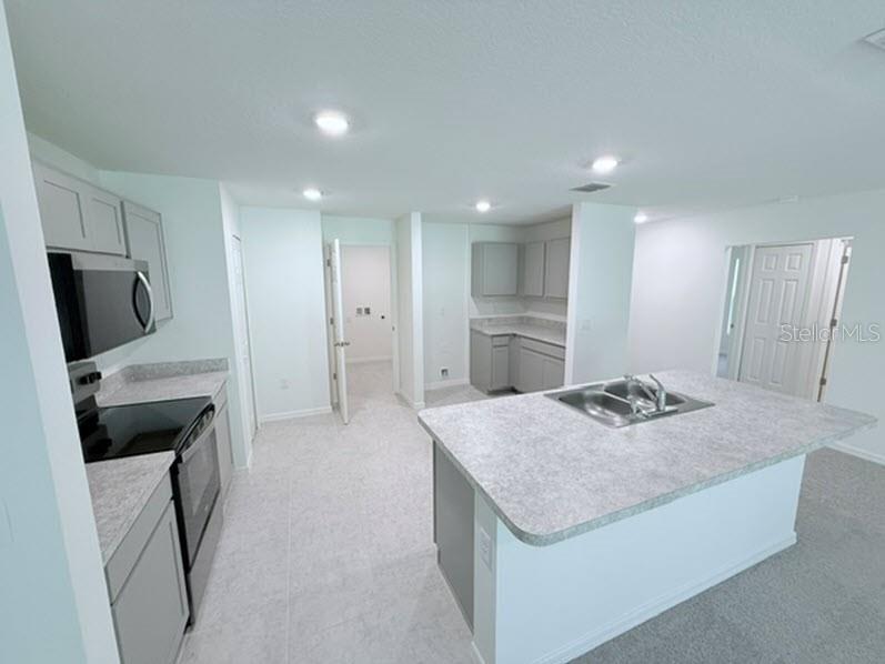 A kitchen features gray cabinets, light countertops, a center island with a sink, and appliances — 40 LAGUNA FOREST TRAIL, PALM COAST, FL