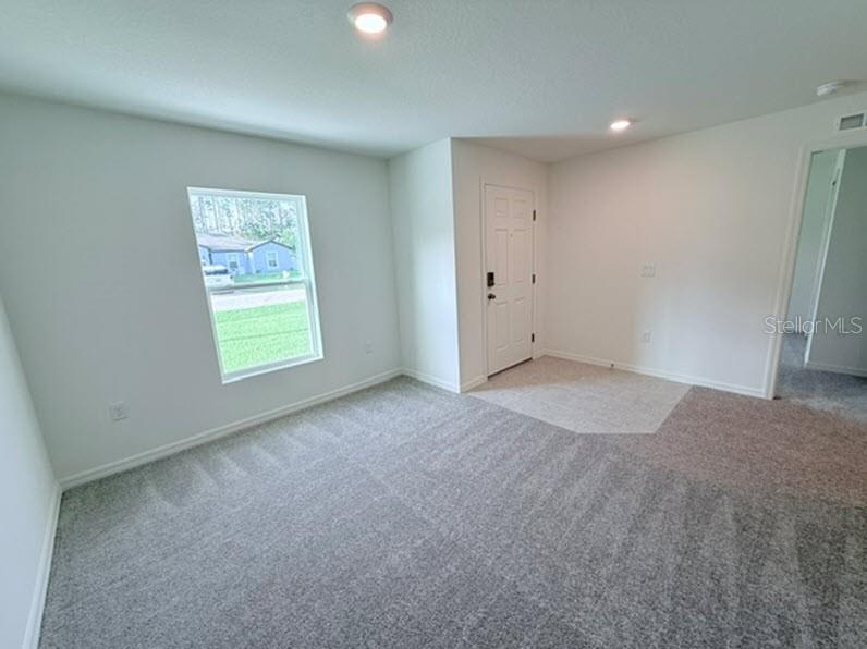 A carpeted room with a window, a white door, and a doorway leading to another area — 40 LAGUNA FOREST TRAIL, PALM COAST, FL