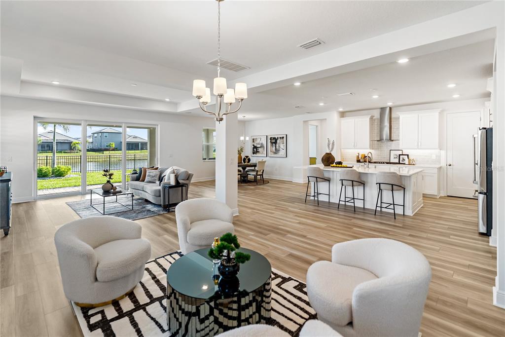 A bright, open-concept living area features light wood flooring, modern cream armchairs, and a geometric rug — 4811 HONEY DEW LANE, BRADENTON, FL