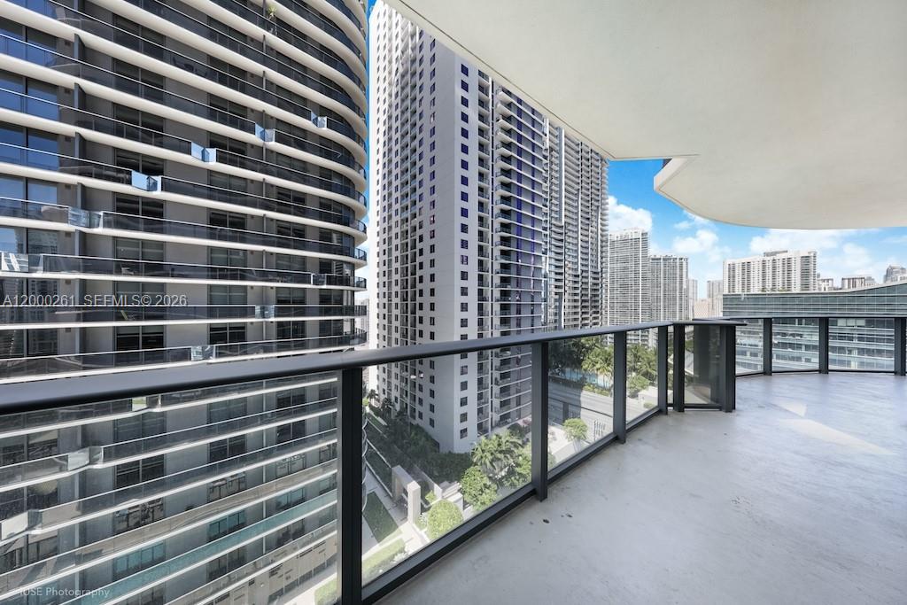 A high-rise balcony with a glass railing overlooks a dense urban landscape of skyscrapers — 45 SW 9th St # 1808, Miami FL 33130, MIAMI, FL