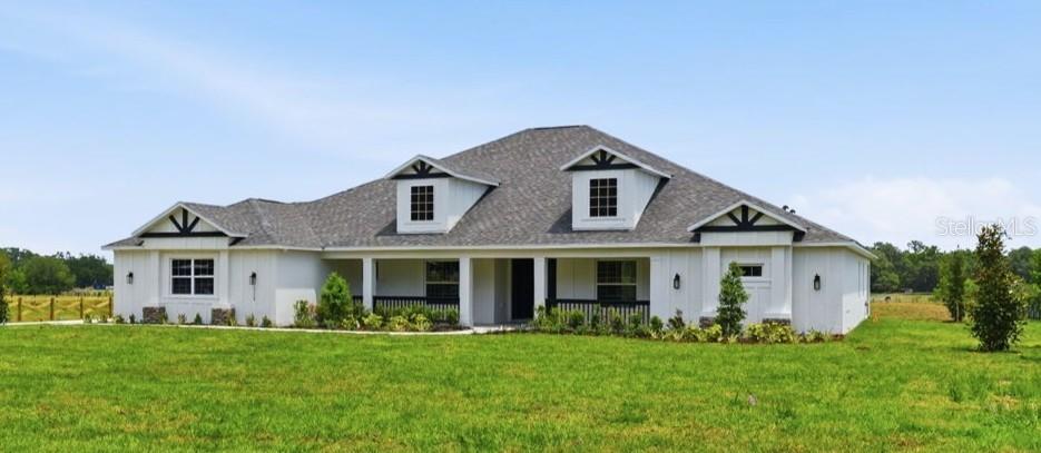 A white farmhouse with a gray roof and a covered front porch sits on grass — 3264 STATION BOULEVARD, BROOKSVILLE, FL