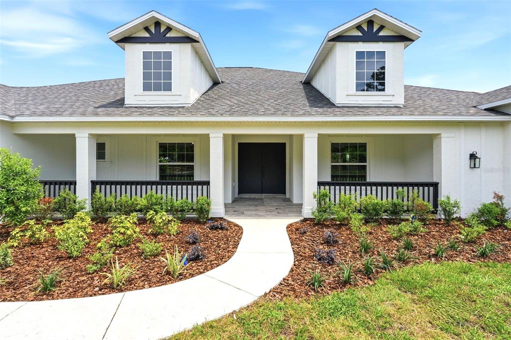 A white house exterior features a covered porch, black railings, and two matching dormer windows — 3264 STATION BOULEVARD, BROOKSVILLE, FL