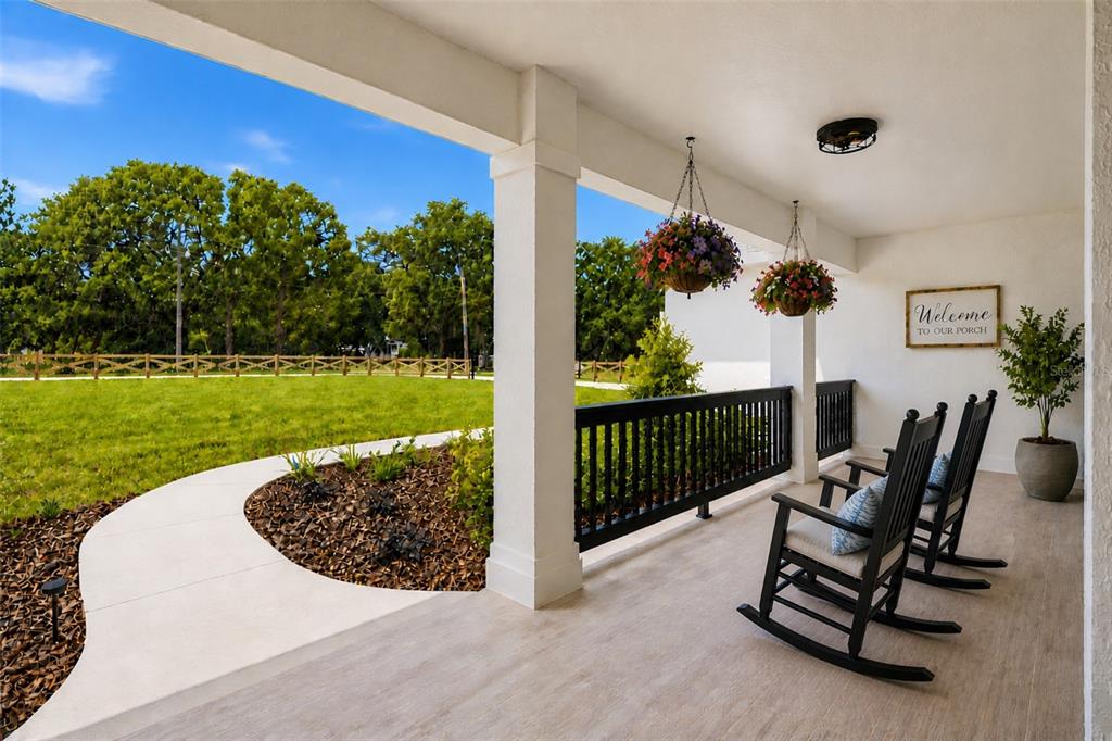 A covered porch features black rocking chairs, hanging flower baskets, and a view of a lawn — 3264 STATION BOULEVARD, BROOKSVILLE, FL