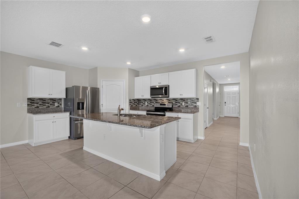 A kitchen features white cabinets, granite countertops, a center island, and tile flooring — 537 TALISI LOOP, ST CLOUD, FL