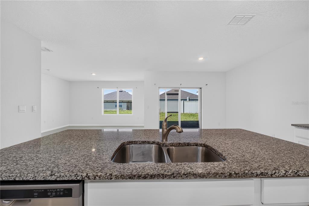 A kitchen island with a double-basin sink and granite countertop overlooks an open living area — 537 TALISI LOOP, ST CLOUD, FL