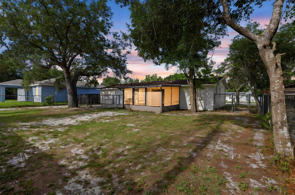 A backyard view of a single-story house with a screened-in porch and mature trees — 2281 CONWAY DRIVE, DELTONA, FL