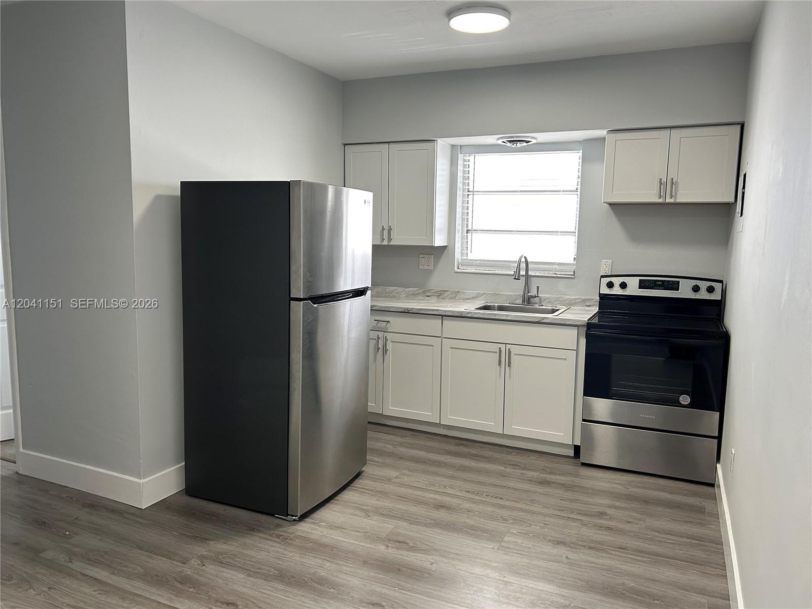 A kitchen features stainless steel appliances, white cabinets, and light-colored wood-look flooring — 1346 Alton Rd # B2, Miami Beach FL 33139, MIAMI BEACH, FL