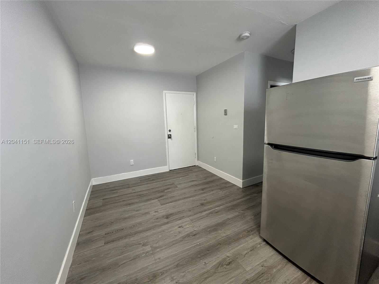 A room with light gray walls, wood-look flooring, a white door, and a stainless refrigerator — 1346 Alton Rd # B2, Miami Beach FL 33139, MIAMI BEACH, FL