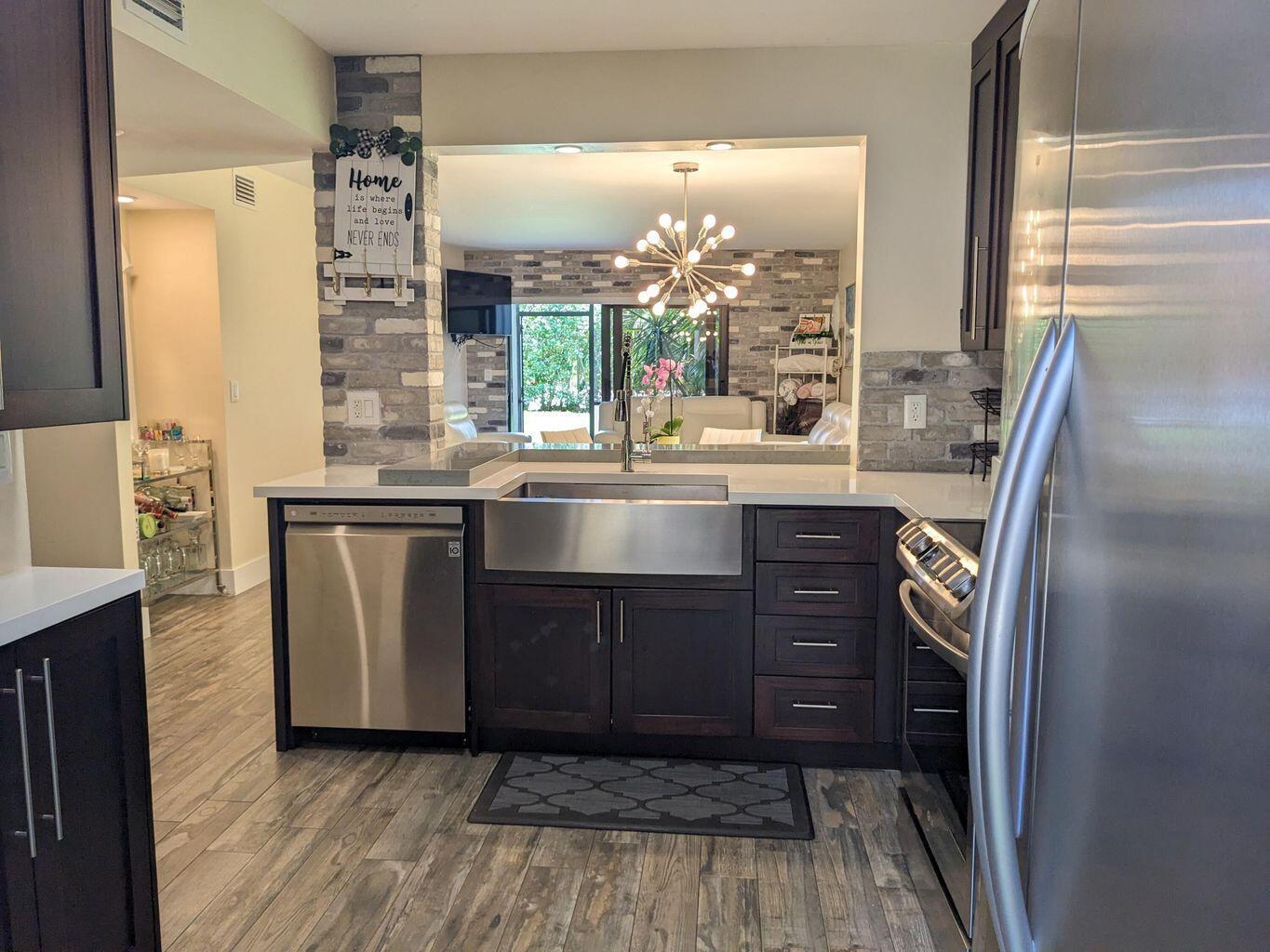 A kitchen features dark wood cabinets, stainless steel appliances, a farmhouse sink, and brick accents — 400 Club Circle # 107, Boca Raton FL 33487, BOCA RATON, FL
