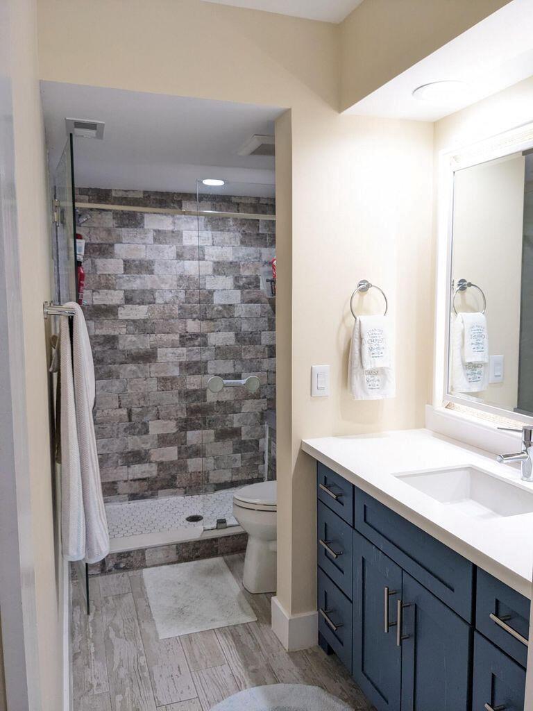 A bathroom features a blue vanity, a white countertop, and a walk-in shower with brick-style tiles — 400 Club Circle # 107, Boca Raton FL 33487, BOCA RATON, FL