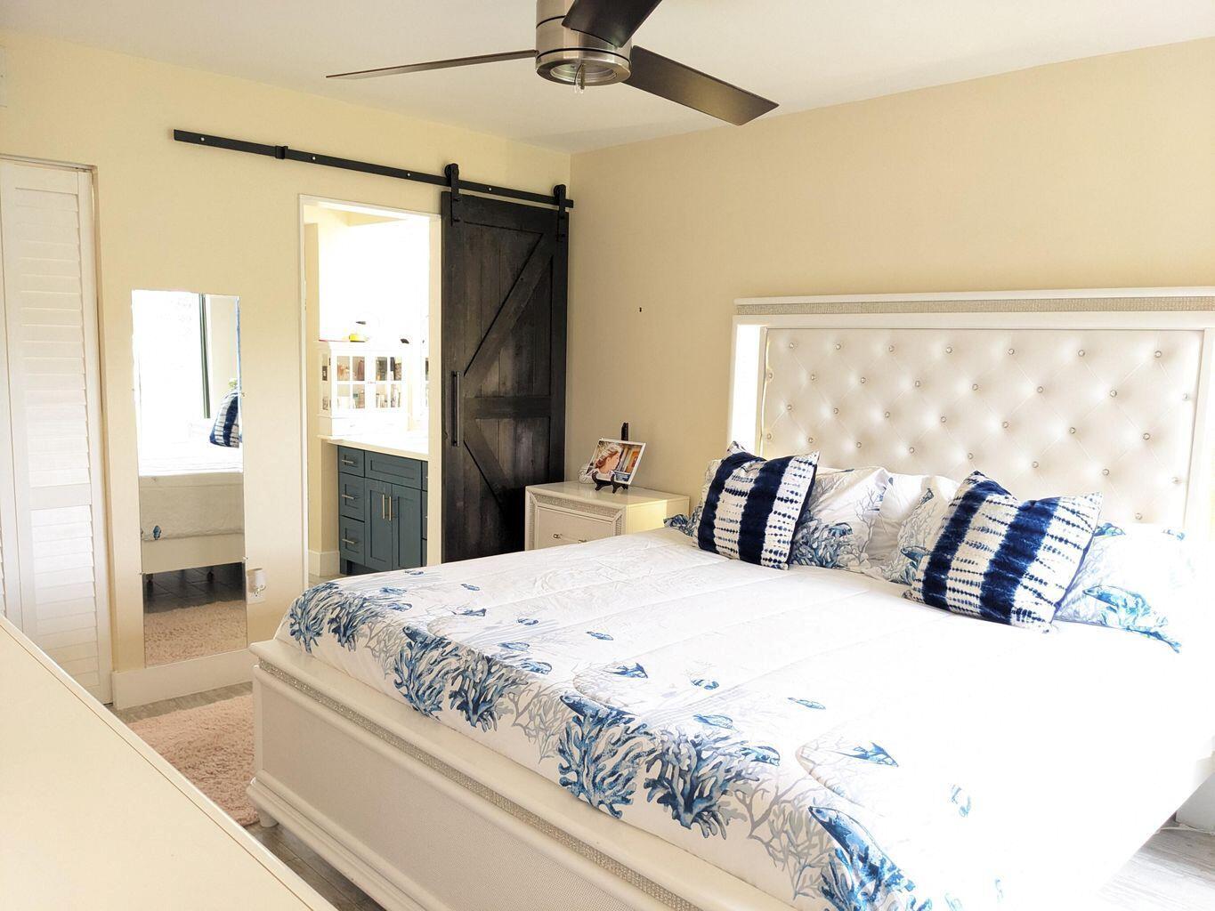 A bedroom with a tufted white headboard, coastal bedding, and a dark sliding barn door — 400 Club Circle # 107, Boca Raton FL 33487, BOCA RATON, FL