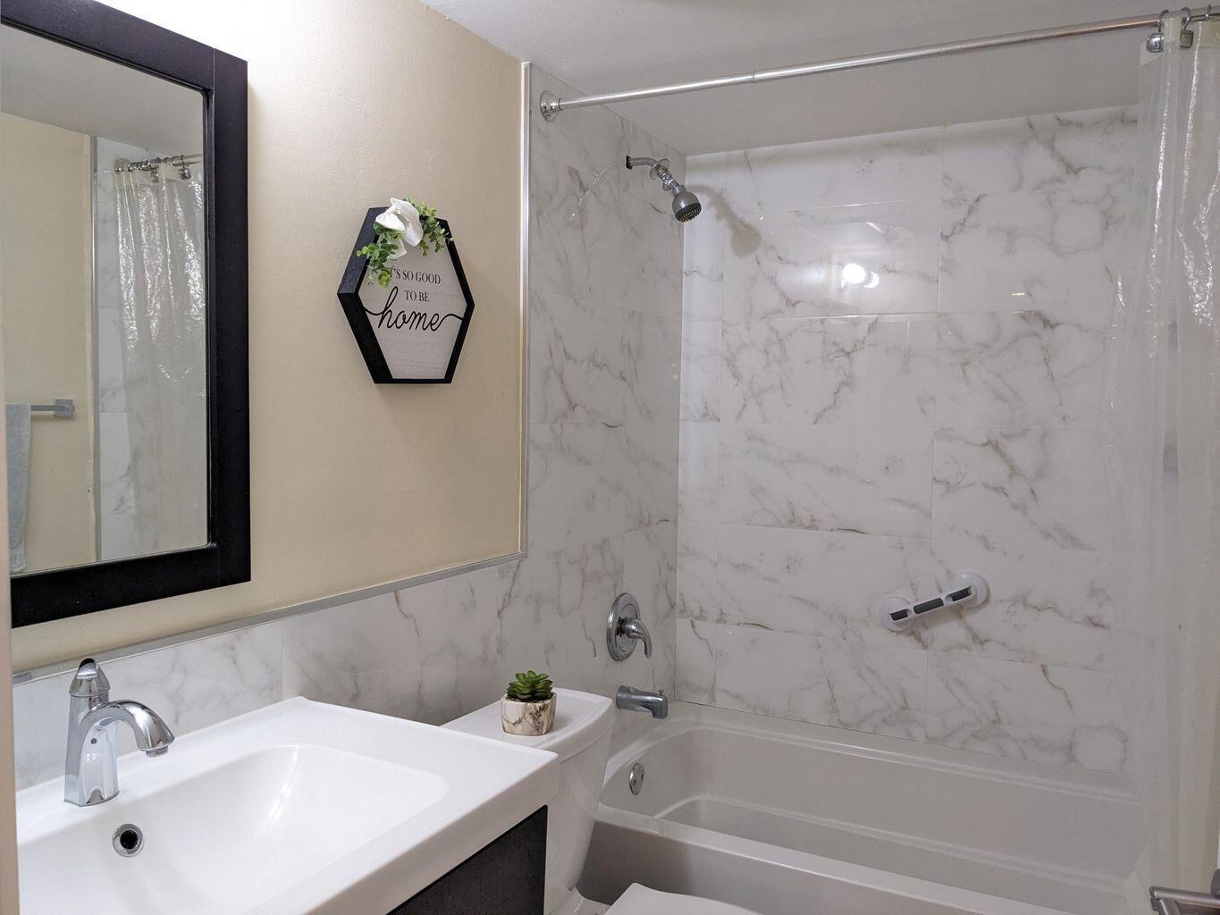 A bathroom features a white vanity, a toilet, and a bathtub with marble-look tile walls — 400 Club Circle # 107, Boca Raton FL 33487, BOCA RATON, FL